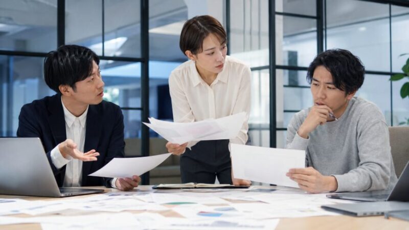 方針や説明が二転三転し、資料を見ながら話し合う日本人の会社員